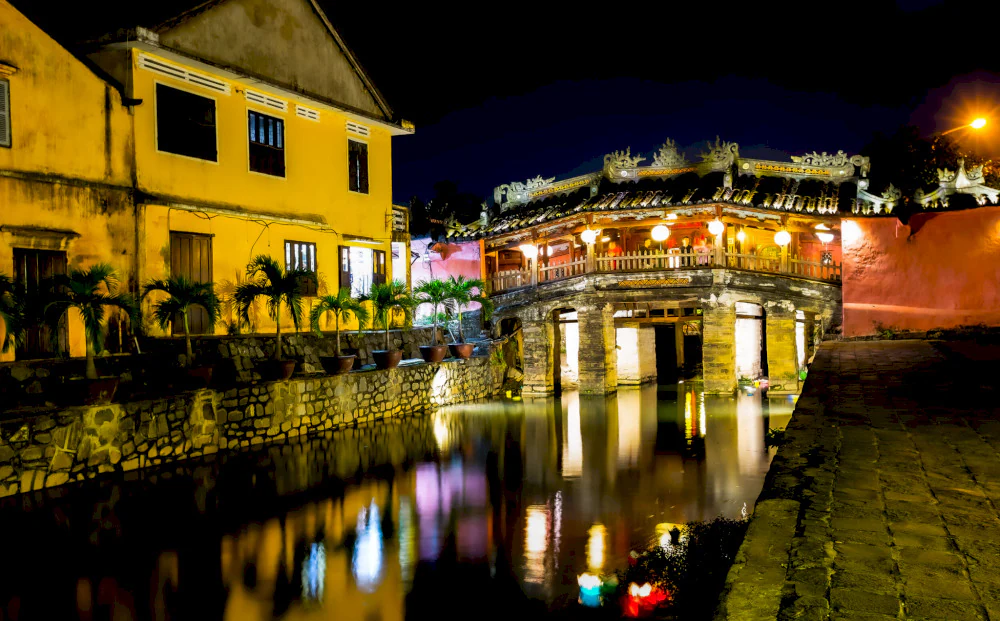 Japanese Covered Bridge glowing at night with colorful lanterns reflected on the river.