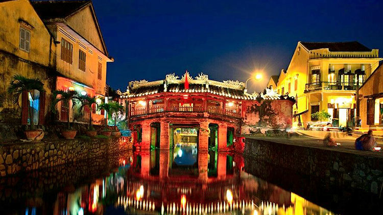 A panoramic view of Hoi An’s Old Town at night, showcasing the Japanese Covered Bridge and lantern-lit streets.